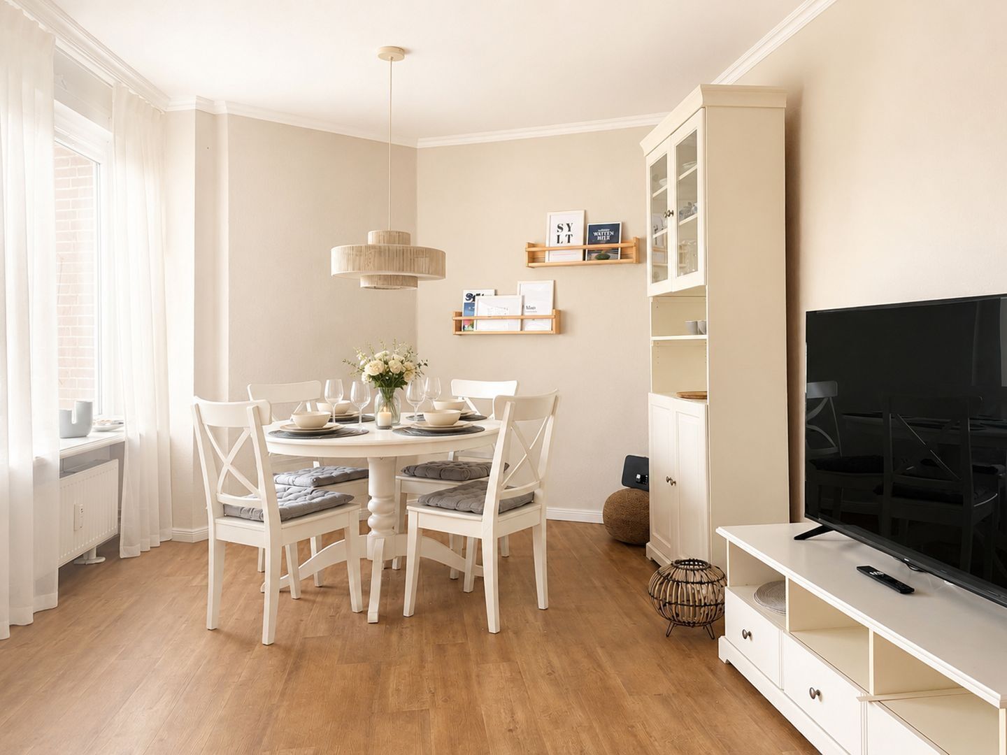Ein Essbereich mit einem runden Tisch, weißen Stühlen und einem Fernseher auf einem Schrank.