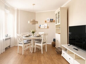 A dining area with a round table, white chairs, and a television on a stand. - Cabin 37 - Cabin 37 – Modern vacation home with a large balcony in Westerland (Sylt)