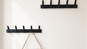 Ein schwarzer, an der Wand befestigter Kleiderhaken mit Haken und einer aufhängbaren gewebten Tasche.