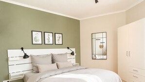 Ein Schlafzimmer mit einem weißen Bett, grünen Wänden und einem weißen Kleiderschrank.