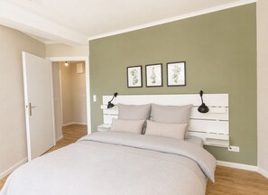 A bedroom with a bed, two bedside lamps, a white headboard, and a green wall. - Cabin 37 - Cabin 37 – Modern vacation home with a large balcony in Westerland (Sylt)