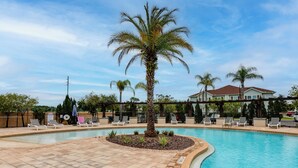 Piscina com espreguiçadeiras e uma palmeira, cercada por uma grade e um prédio ao fundo.