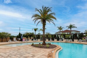 Ein Pool mit Liegestühlen und einer Palme, umgeben von einem Zaun und einem Gebäude im Hintergrund.