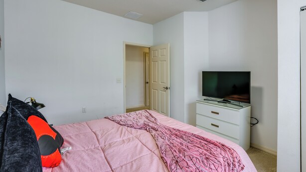 Quarto com uma cama, televisão sobre um suporte, uma porta e um guarda-roupa.