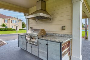Eine Außenküche mit Edelstahlgrill, Dunstabzugshaube und einer Arbeitsplatte aus Granit.