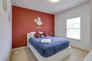 Ein Schlafzimmer mit einem Bett, einem Fenster und einer Wand mit einem Mickey Mouse Plakat.