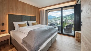 Un dormitorio moderno con una cama grande, paneles de madera y un balcón con vistas a un pueblo y colinas.