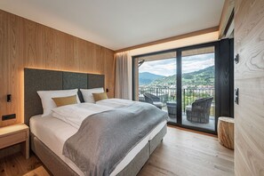 Een moderne slaapkamer met een groot bed, houten lambrisering en een balkon met uitzicht op een stad en heuvels.