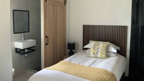 Une chambre à coucher avec un lit, une table de chevet avec une lampe, une armoire en bois et une salle de bain avec un lavabo et un miroir.