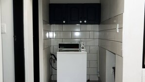 Une cuisine de taille réduite, avec un réfrigérateur blanc, un four à micro-ondes et des meubles de rangement de couleur foncée.