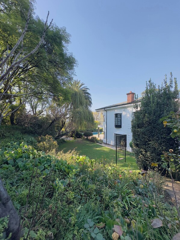 A white building with a visible door and windows, surrounded by lush greenery and trees.