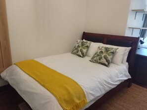 A bed with white bedding and two pillows, a yellow throw blanket, and a wooden headboard.