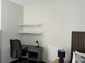 Una habitación pequeña y moderna con escritorio, silla y estanterías.