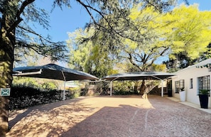 An outdoor patio area with brick flooring, covered seating areas, and a building with windows.