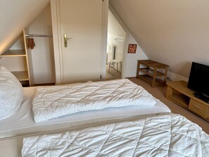 Ein Schlafzimmer mit einem Bett, einem Nachttisch aus Holz, einem Fernseher und einer Tür zu einem Badezimmer.