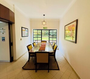 A conference room with a long table, chairs, a rug, a chandelier, and large windows with a view of greenery. - Single Self-Contained Rooms (Johannesburg)