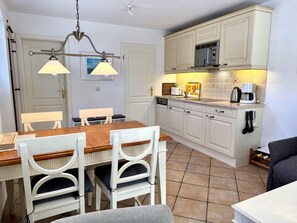 A compact kitchen with white cabinetry, a dining table with chairs, and a ceiling fan. - Norderstraße, Apartment 2 - Cozy ground-floor vacation apartment with a south-facing terrace in (Sylt)