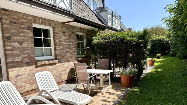 En terrasse med hvide liggestole, et bord og plantekrukker.