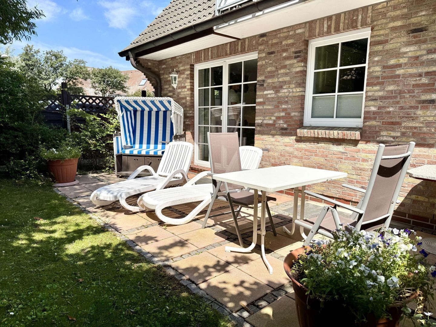 A patio with a table and chairs, a striped beach chair, and a potted plant.