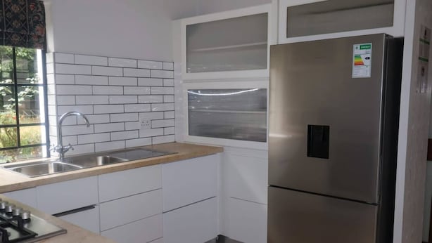 Una cocina con armarios blancos, un refrigerador de acero inoxidable, una ventana y un lavamanos.