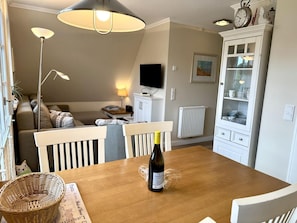 A dining area with a wooden table, a bottle of wine, and a basket. - Eidumweg Apartment 5 - Bright and modern upper-floor apartment for 4 people with (Sylt)