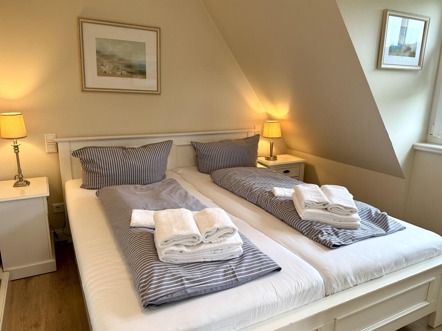 A twin room with two beds, each with striped bedding and pillows, bedside lamps, and a framed picture on the wall.