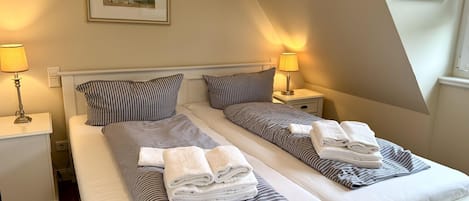Une chambre double avec deux lits, chacun doté de draps et d’oreillers à rayures, de lampes de chevet et d’un tableau encadré au mur.