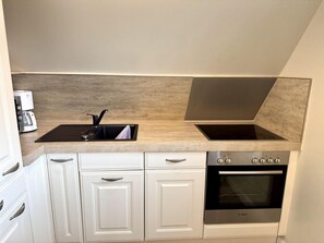A compact kitchen with a built-in stove, oven, and sink. - Eidumweg Apartment 5 - Bright and modern upper-floor apartment for 4 people with (Sylt)