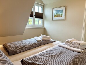A bedroom with two beds, a window with blinds, a framed picture on the wall, and towels on the beds. - Eidumweg Apartment 5 - Bright and modern upper-floor apartment for 4 people with (Sylt)