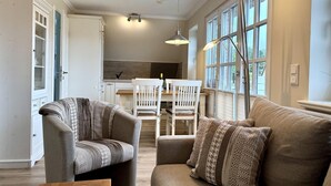 En stue med sofa, to lænestole, spisebord med stole og et køkken i baggrunden.