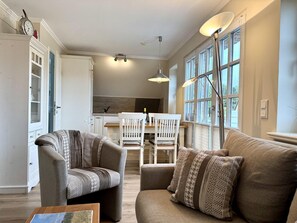 A living room with a sofa, two armchairs, a dining table with chairs, and a kitchen in the background. - Eidumweg Apartment 5 - Bright and modern upper-floor apartment for 4 people with (Sylt)