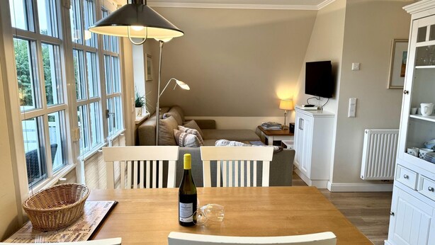 En hyggelig stue med et træbord, hvide stole, en sofa og et fjernsyn.