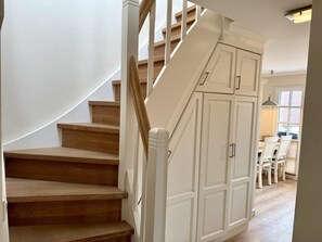A wooden staircase with white walls and a white door leading to a dining area with a table and chairs. - Eidumweg Apartment 5 - Bright and modern upper-floor apartment for 4 people with (Sylt)