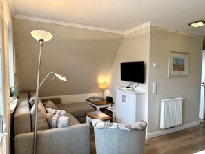 A living room with a sofa, armchairs, a TV, a lamp, a radiator, and a framed picture on the wall. - Eidumweg Apartment 5 - Bright and modern upper-floor apartment for 4 people with (Sylt)