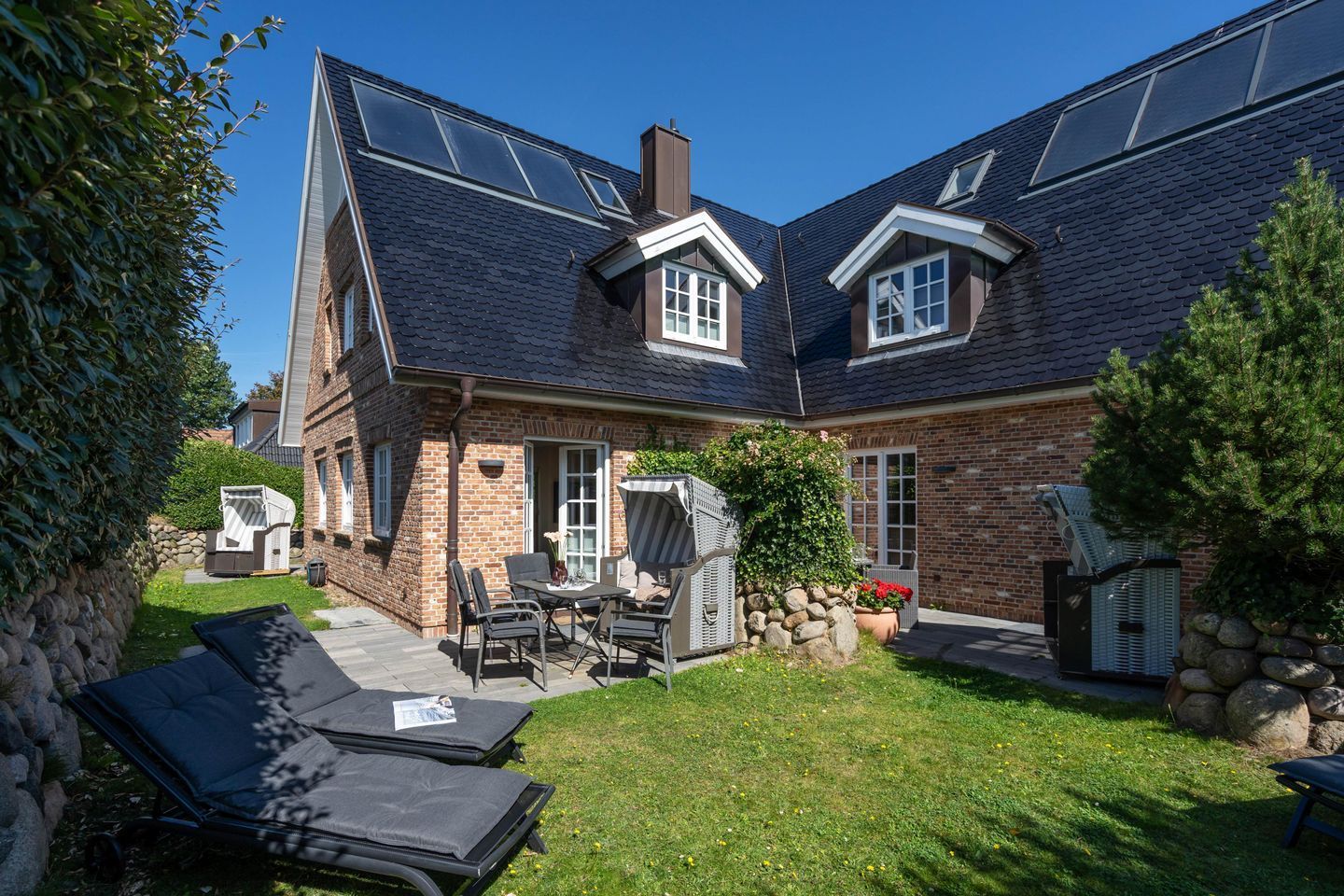 Et toetagers hus med murstensfacade, en overdækket terrasse med udendørs møbler og en have.
