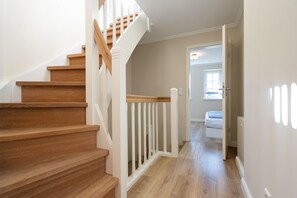 Eine Treppe mit Holzdielen und weißen Geländern führt zu einem Schlafzimmer mit einem Bett und einem Fenster.