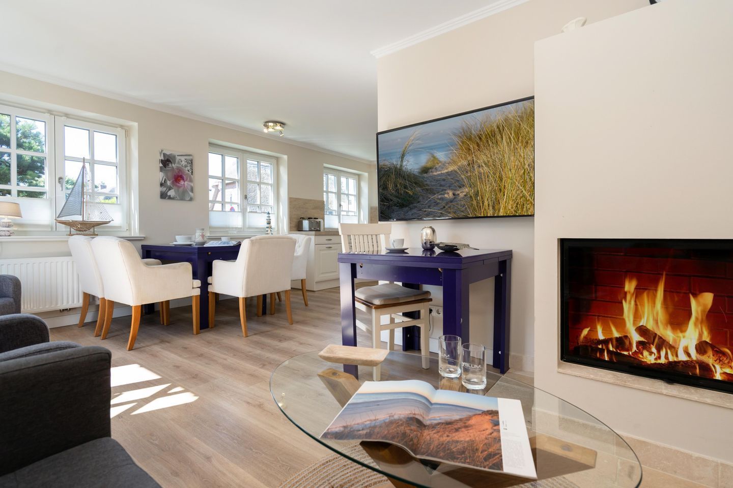 Un salon moderne avec une table basse en verre, une cheminée et un coin repas comprenant une table bleue et des chaises blanches.