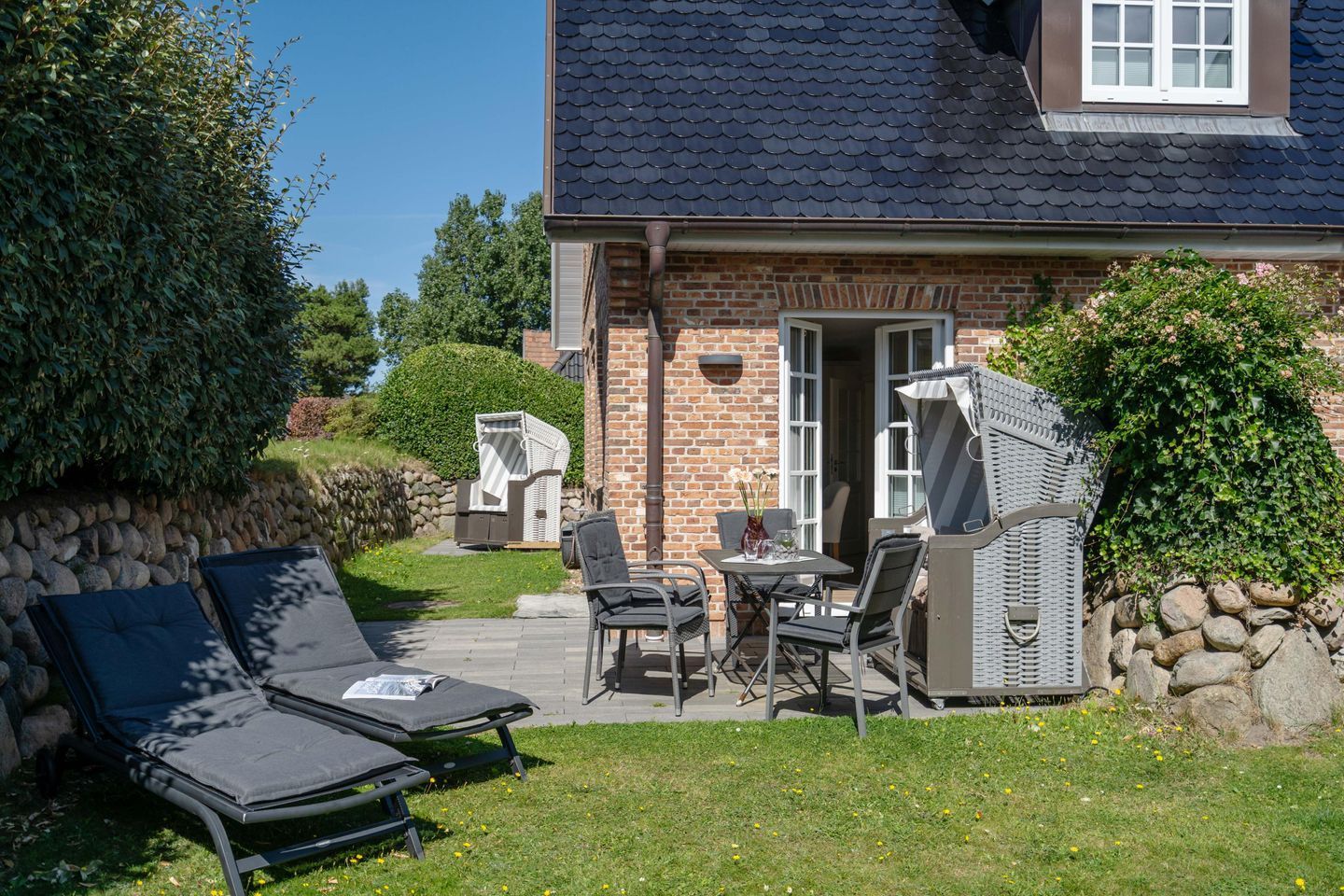 Ein Backsteinhaus mit Ziegeldach, einer Steinmauer und einer Terrasse mit Gartenmöbeln.