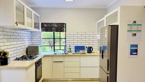 Een keuken met witte kastjes, een gasfornuis, een spoelbak en een koelkast.