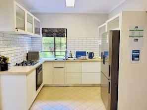 Cocina con alacenas blancas, estufa a gas, pileta y refrigerador.