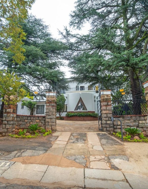 A gated entrance with stone walls and metal gates, leading to a building with a triangular window and a stone base.