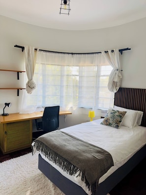 A bedroom with a bed, desk, chair, and a window with curtains.