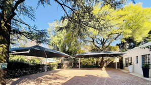 An outdoor patio area with brick flooring, covered seating areas, and a building with windows. - Double Self-Contained Rooms 2 (Johannesburg)
