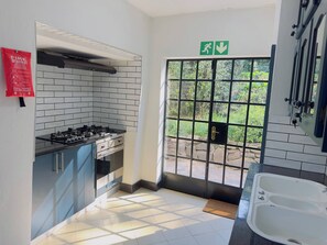 Una cocina con estufa a gas, armarios, una manta ignífuga y vistas a un área exterior a través de una puerta.