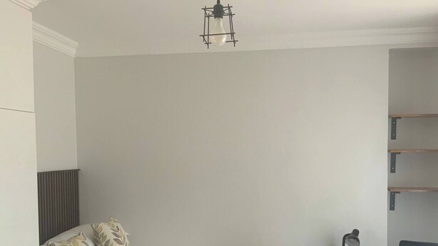 Una cama individual con cabecera, una mesita de noche con lámpara, una silla y un tapete tejido sobre piso de madera.