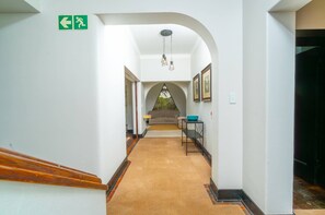 A hallway with a carpeted floor, a staircase, a sofa, a table with a bowl, framed pictures on the wall, and an exit sign.