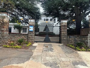 A gated entrance with a stone wall, a metal gate, and a sign indicating armed response and 24/7 CCTV.