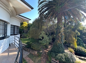 A modern building with a curved balcony, a palm tree, and a well-maintained garden with various shrubs and a pathway.