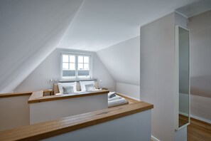 Ein modernes Schlafzimmer im Dachgeschoss mit schrägen Wänden, integriertem Fenster, einer Holzbank und einem Bett mit Kissen.