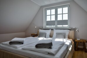 Ein Schlafzimmer mit einem großen Bett, zwei Nachttischen, einem Fenster mit Jalousien und einer schrägen Decke.